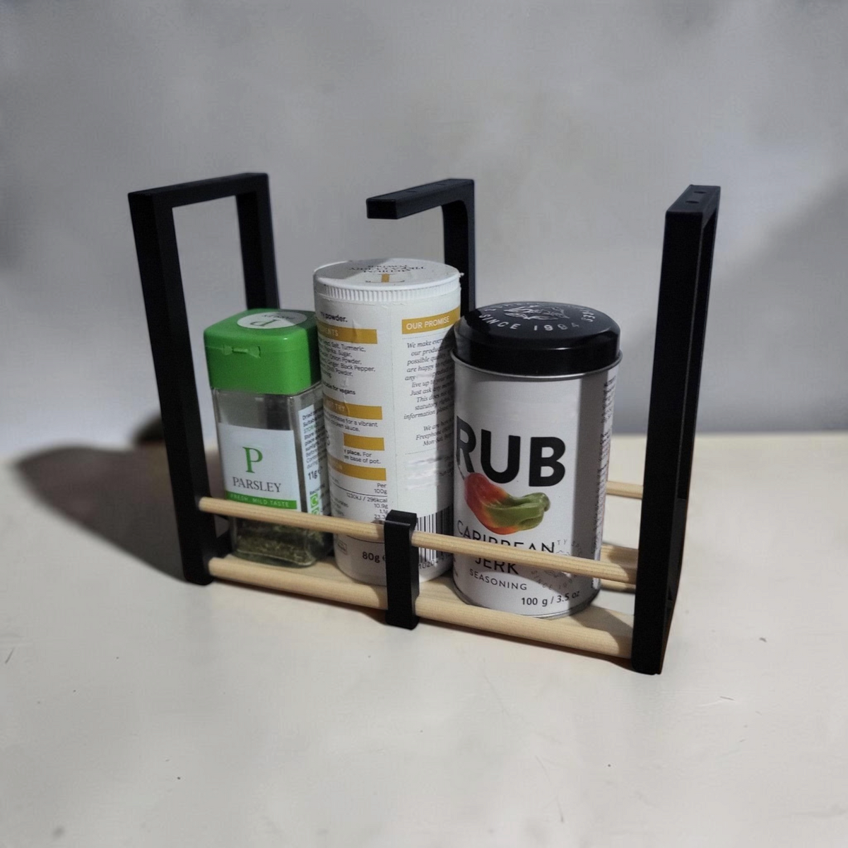 Countertop view of a black spice rack kit assembled with wooden dowels and filled with assorted spice jars.