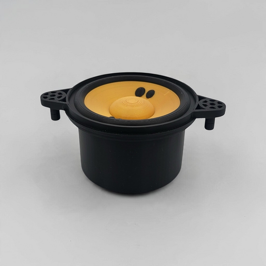 Black fake speaker storage cup with a yellow speaker cone, shown on a wooden surface.