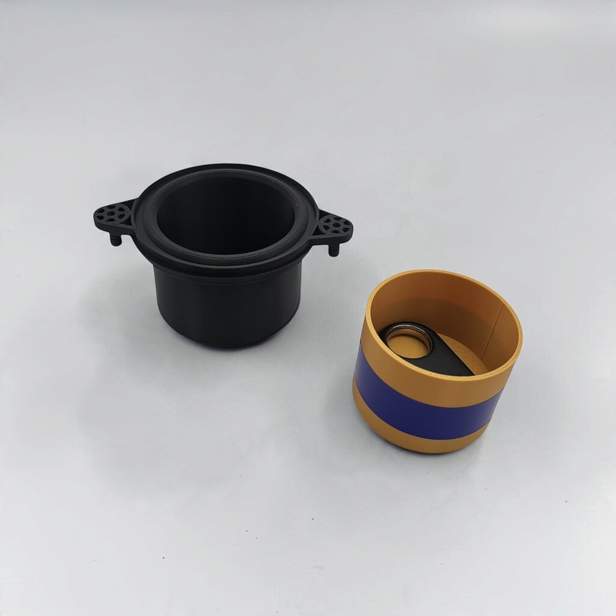Open black storage cup shown beside a small yellow and blue container.