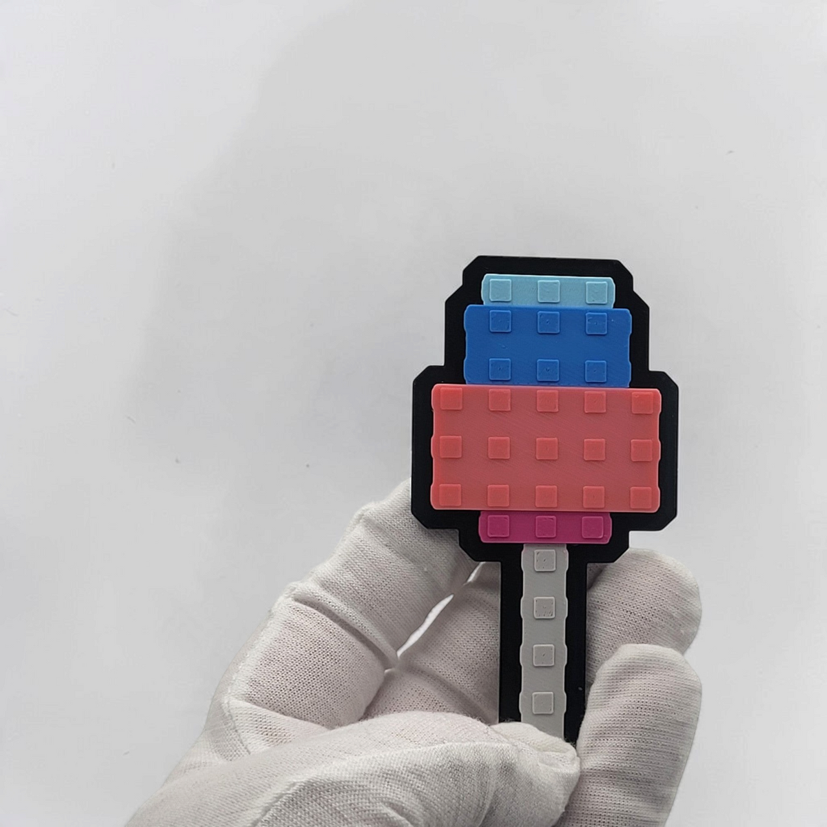 Gloved hand holding a blue and pink pixel-style Candy Blossom fridge magnet for scale.