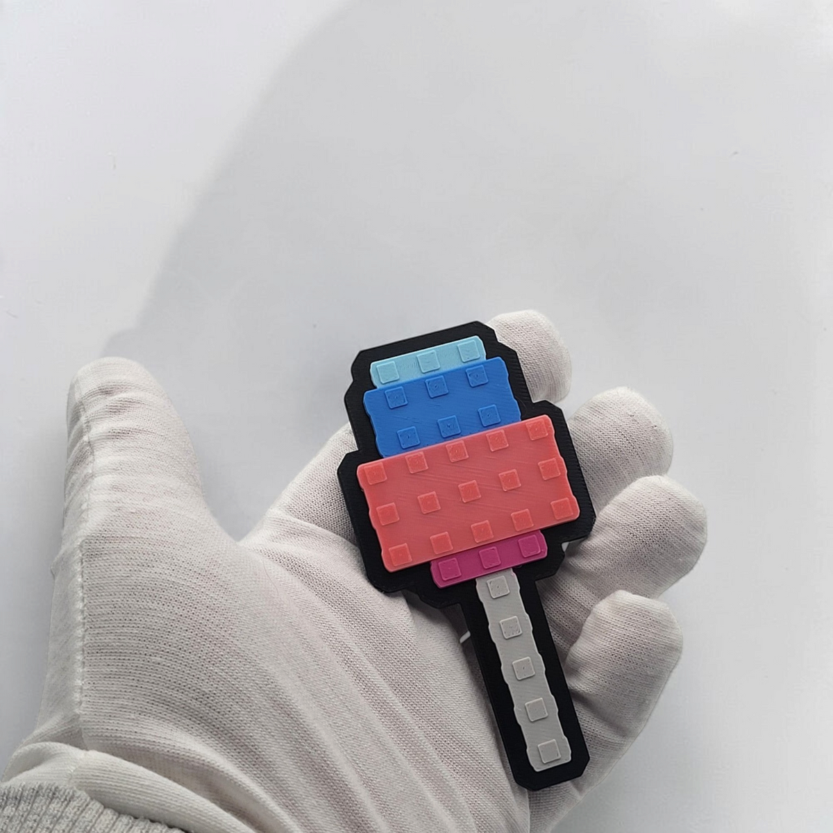 Candy Blossom pixel popsicle magnet held in a gloved hand, showing its black backing and grey handle.
