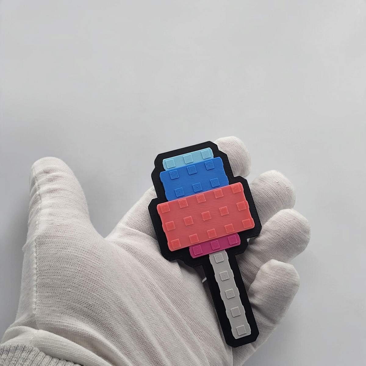 Blue and pink pixelated Candy Blossom badge held in a white gloved hand for scale.