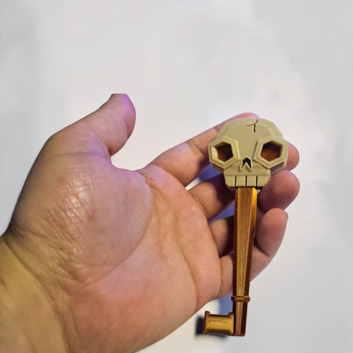 Close up of a hand holding a gold and bronze 3D printed skeleton key with a detailed skull shaped bow.