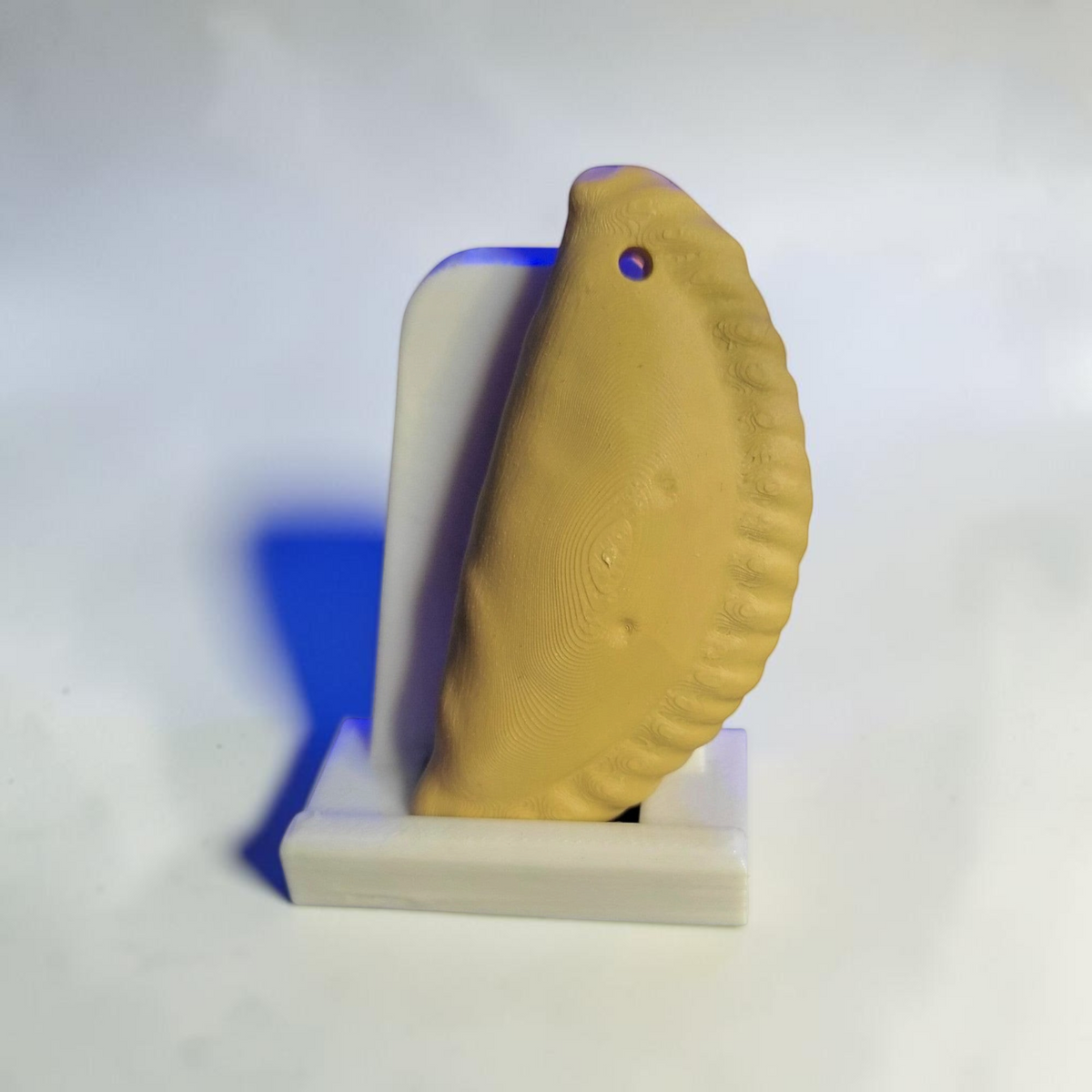 ARt Cornish Pasty Keyring in a golden-brown pastry colour with a crimped edge design on a white display stand.