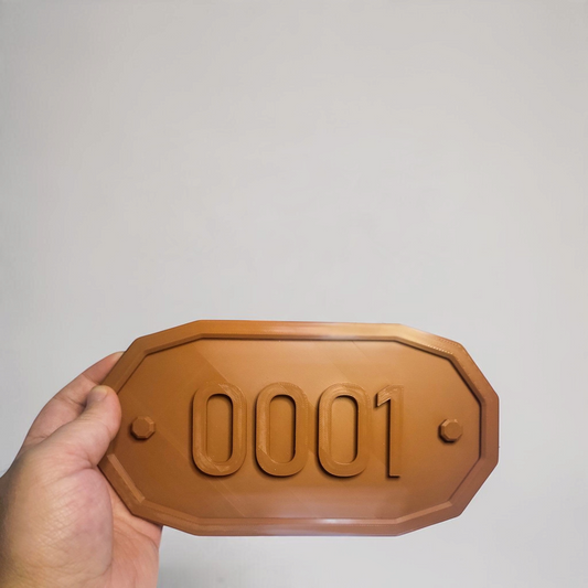 Hand holding a brown custom room number sign with raised digits on an octagonal plaque, shown close up.