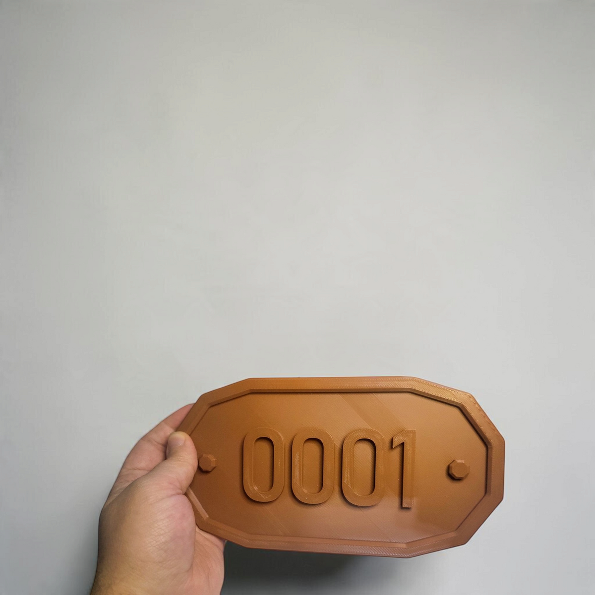 Hand holding a brown gaming room number plaque with customizable raised digits and a smooth rectangular design.
