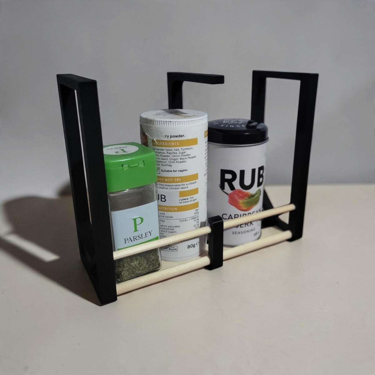 Assembled DIY spice rack with black 3D printed side brackets, wooden dowels and spice jars on a white countertop.