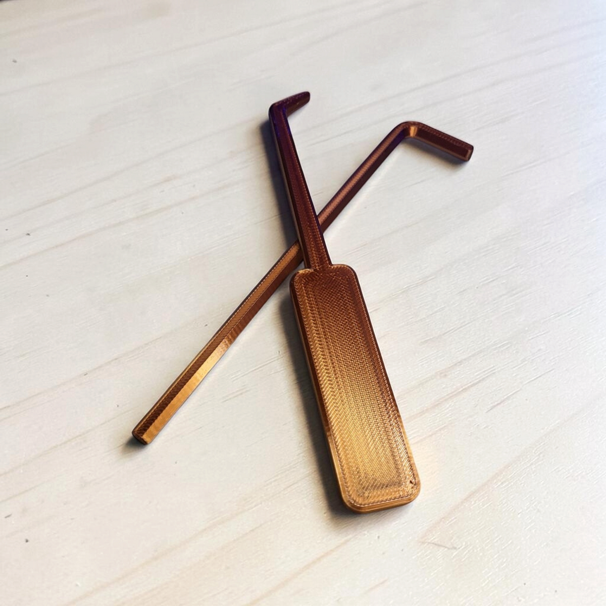 Two copper-colored Doors Inspired lockpick props with textured handles arranged on a light wooden surface.