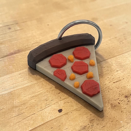 Doors-inspired pizza slice keychain with brown crust, beige cheese, red pepperoni, and a silver key ring on a wooden table