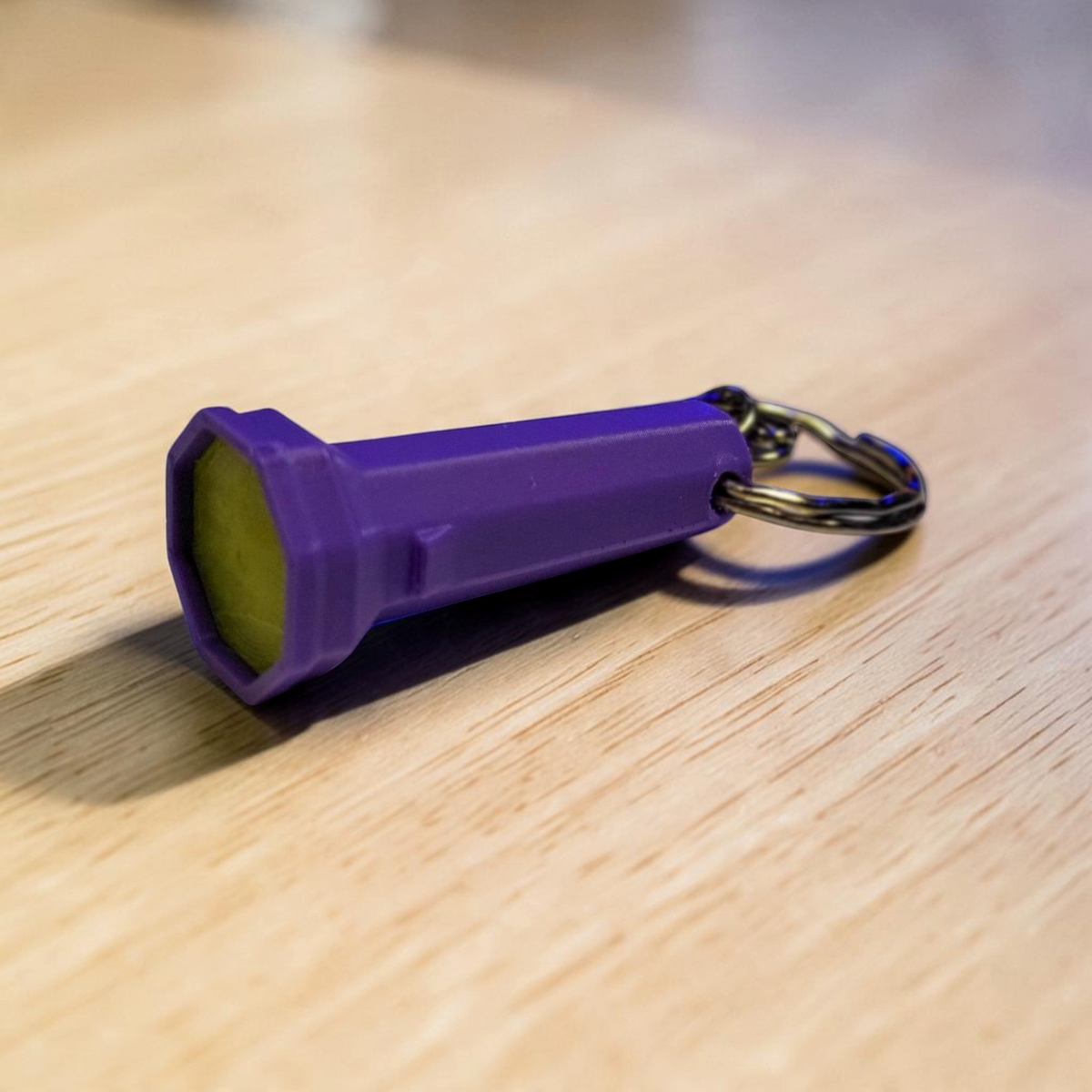 Purple flashlight keyring with a yellow green lens and metal ring, resting on a wooden surface.