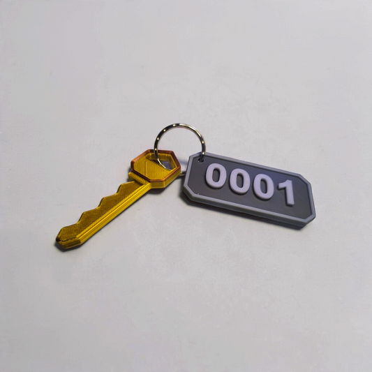 Gold key attached to a grey number 0001 room key tag on a keyring, shown on a light surface.