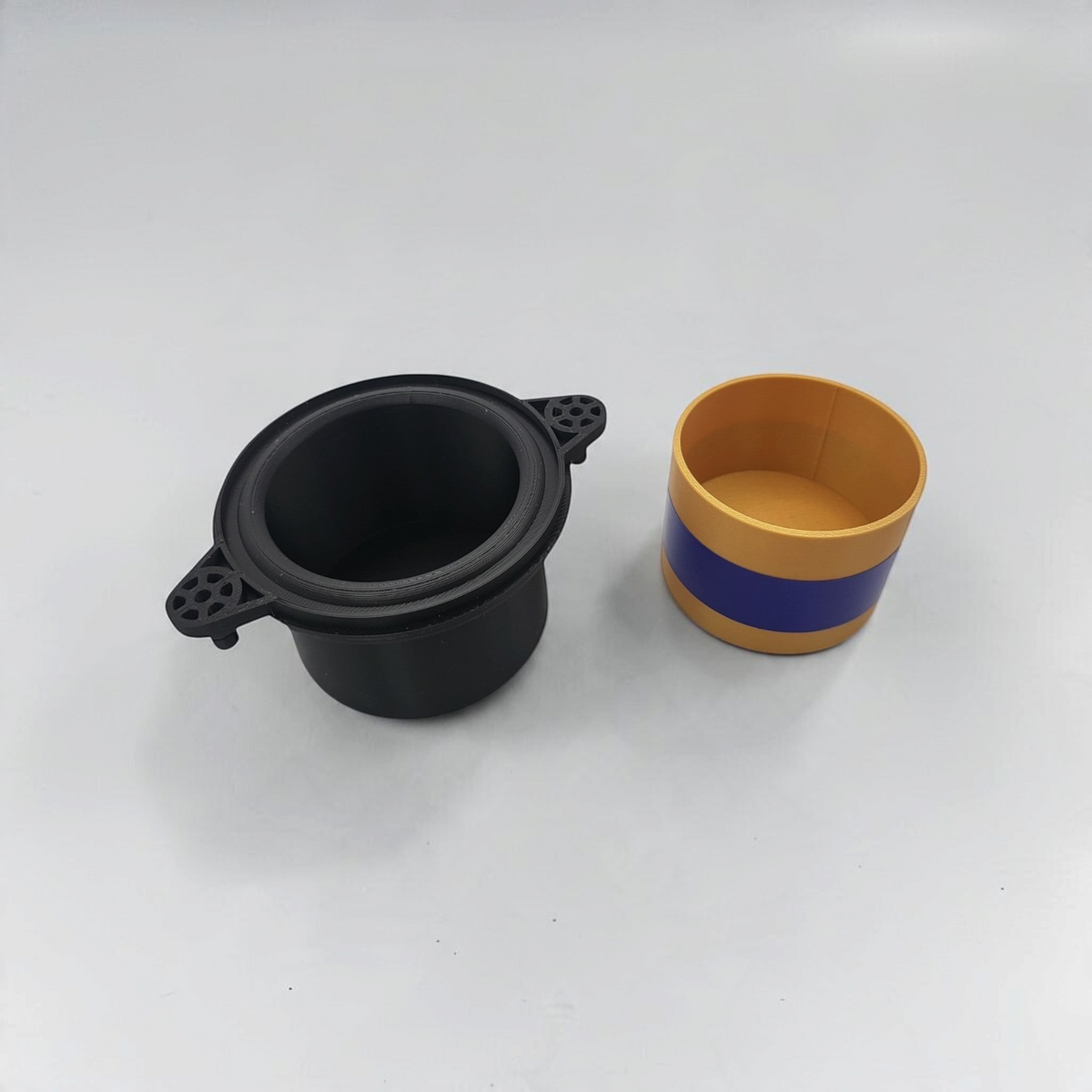 Black open speaker-style storage cup shown beside a yellow and blue insert container.