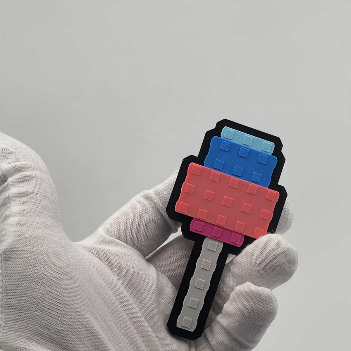 Gloved hand holding a blue and pink pixel-style Candy Blossom badge with a grey handle.