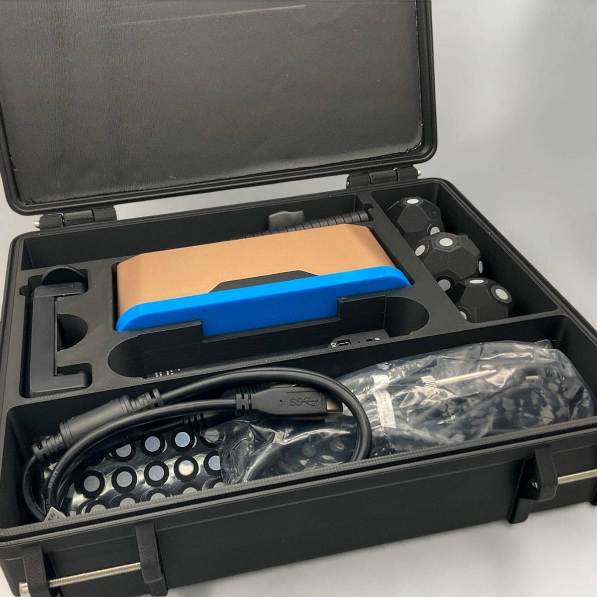 Close view of an open scanner case with blue and orange equipment, cables and accessories in fitted foam compartments.