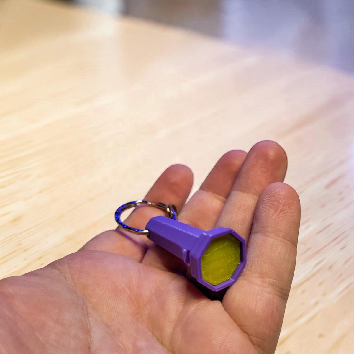 Close view of a purple flashlight keyring and yellow green lens resting in a hand.