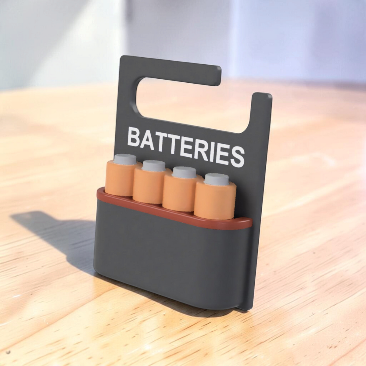 Front angled view of a black 3D-printed battery holder labelled “BATTERIES”, with four copper-coloured batteries arranged in a row.