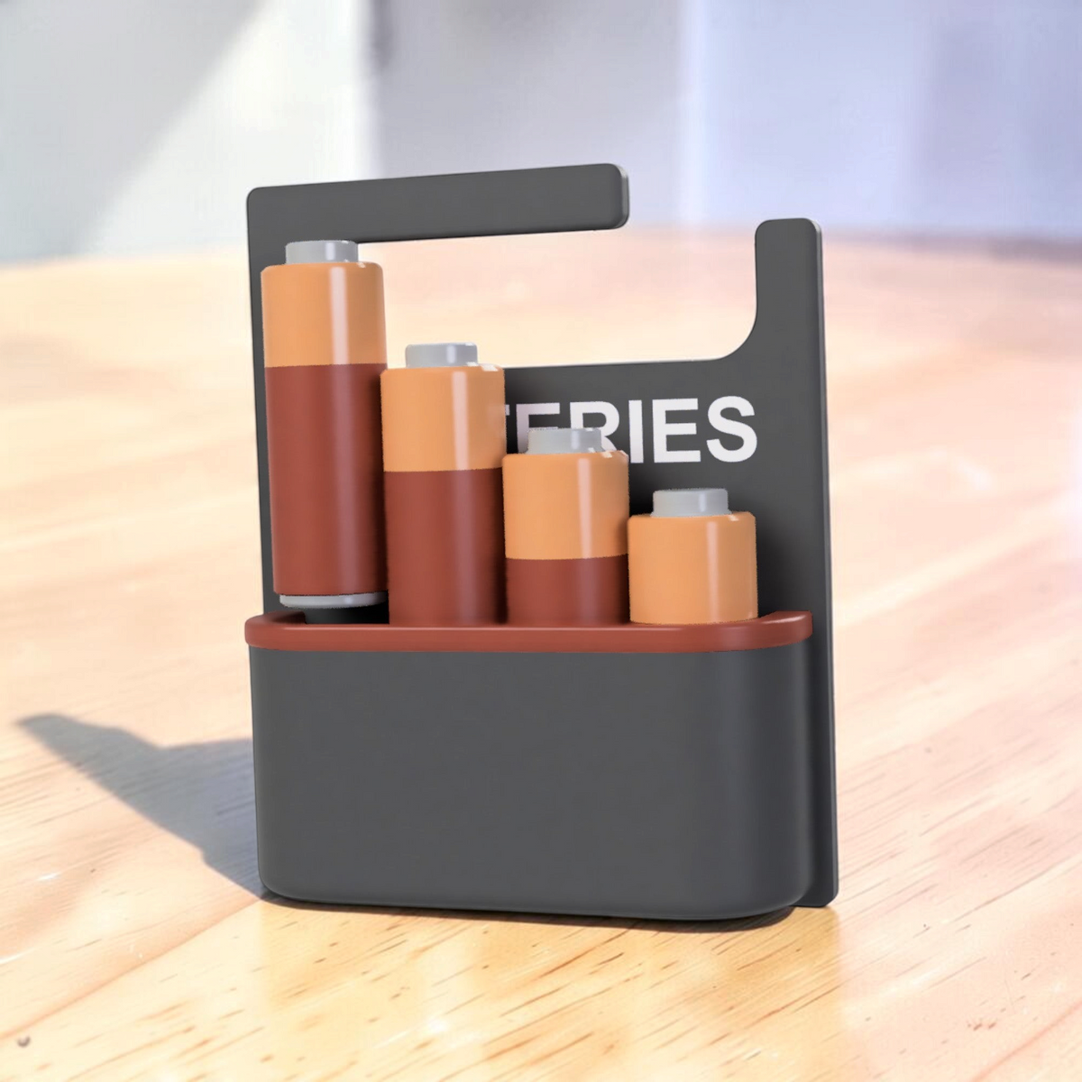 Front view of a black 3D-printed battery holder labelled “BATTERIES”, displaying copper-coloured batteries in different sizes.