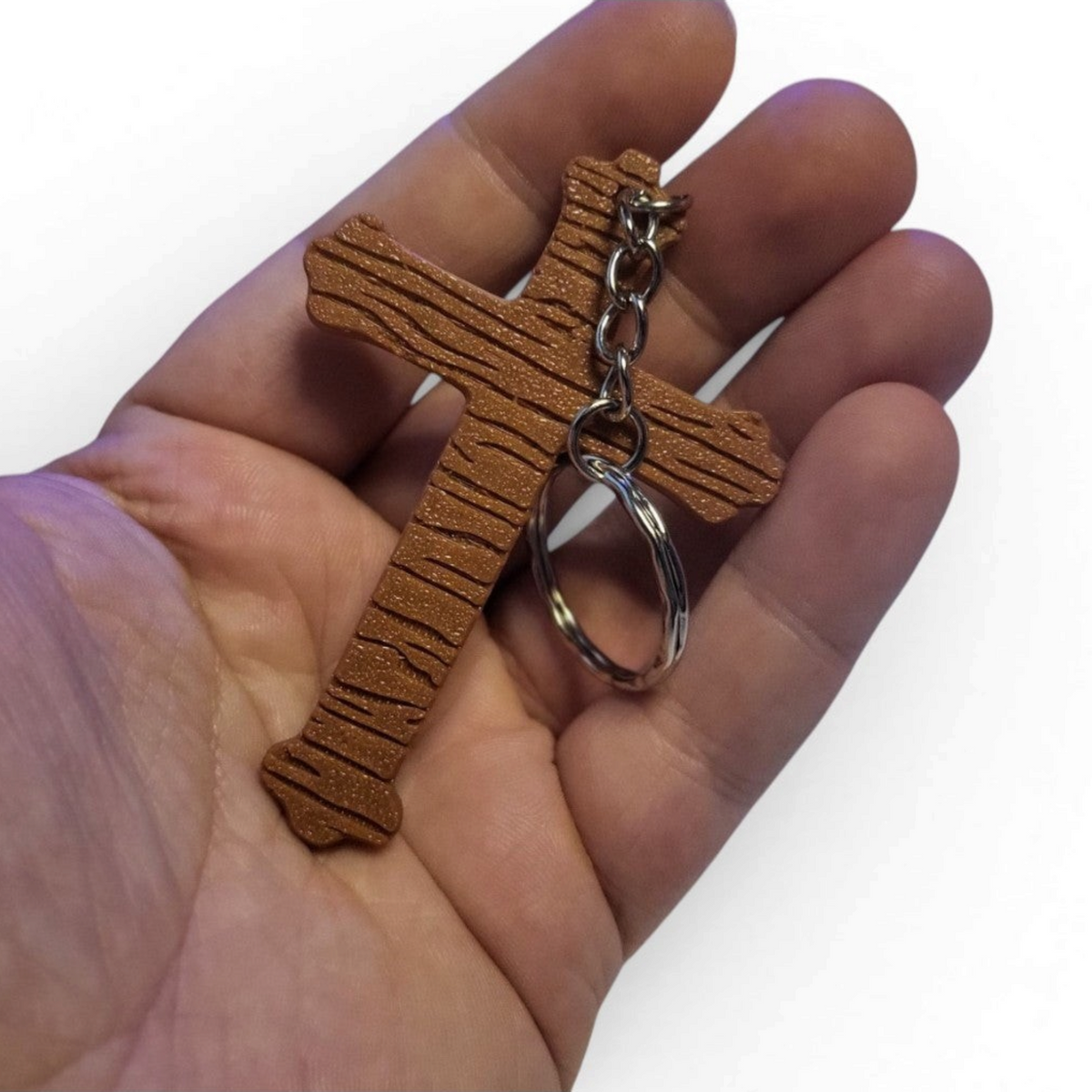 Brown textured Doors-inspired crucifix keychain shown held in a hand for scale.