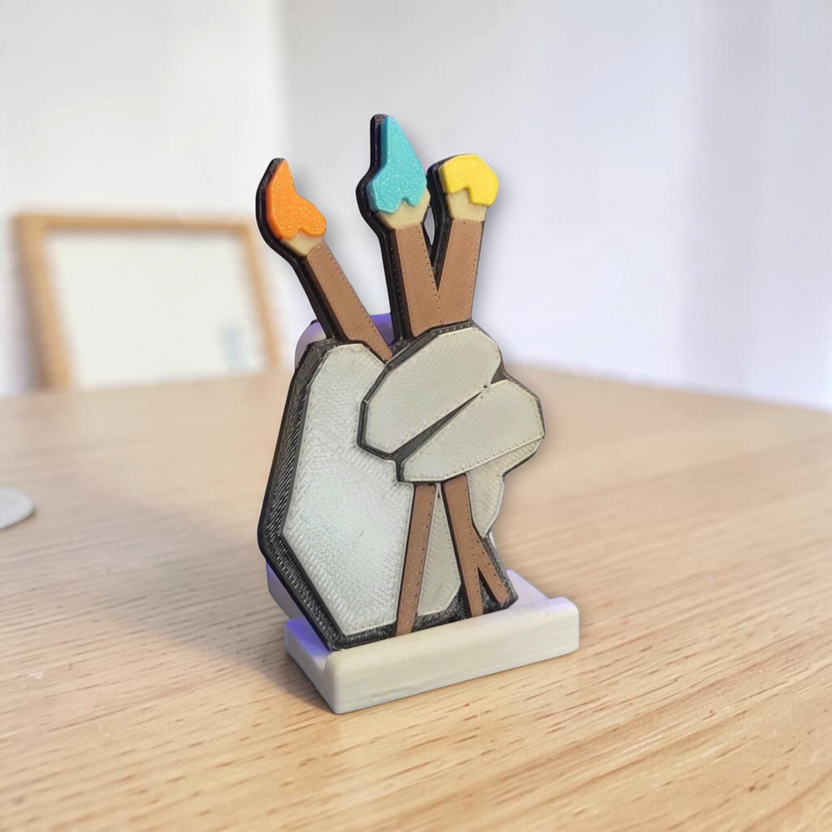 Gorilla Tag illustrator badge fan art with a hand holding three paintbrushes on a wooden table.