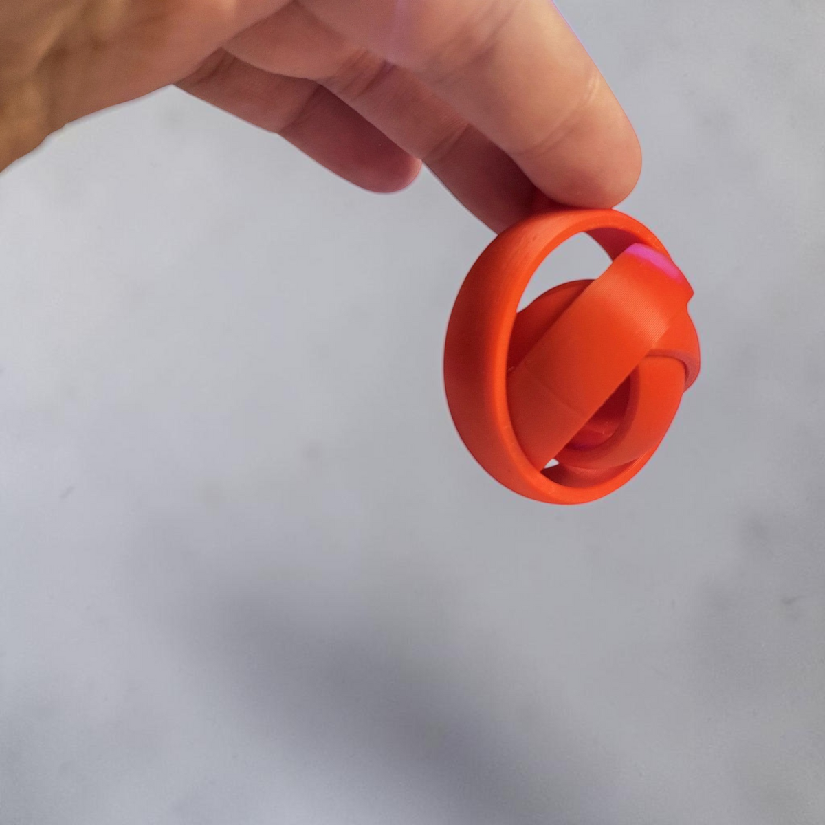 Orange 3D printed gyro keyring held between fingers.