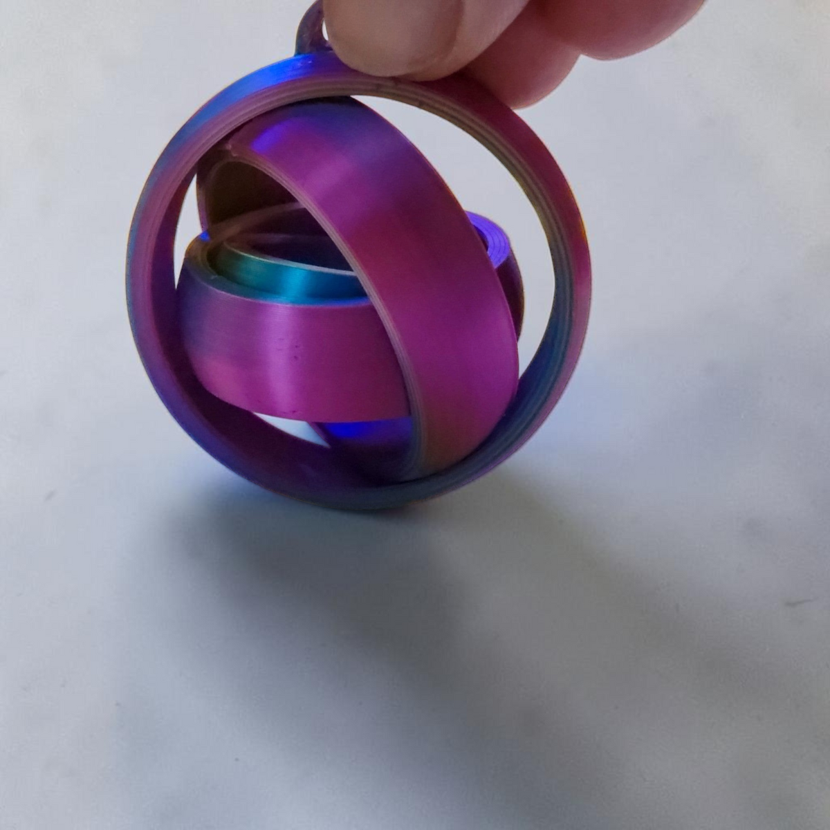 Rainbow 3D printed gyro keyring held between fingers against a white background.